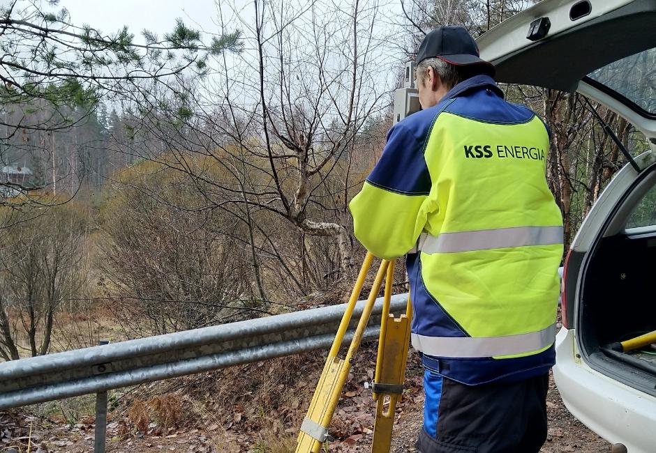 Henkilö KSS Energian huomiotakissa kurkistaa jalustalla seisovan mittauslaitteen läpi.